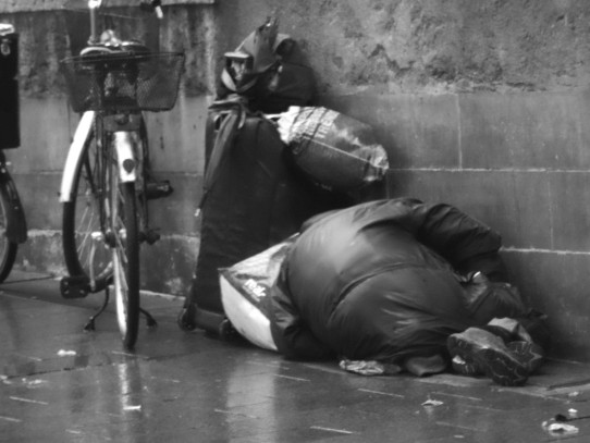 Obdachloser schläft auf dem Pflaster im Regen