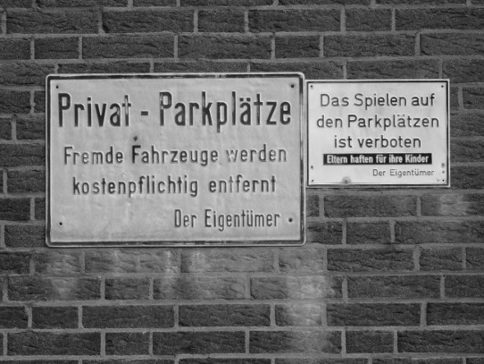 Zwei Schilder: 'Privat-Parkplätze Fremde Fahrzeuge werden kostenpflichtig entfernt Der Eigentümer' 'Das Spielen auf den Parkplätzen ist verboten/ Eltern haften für ihre Kinder Der Eigentümer'