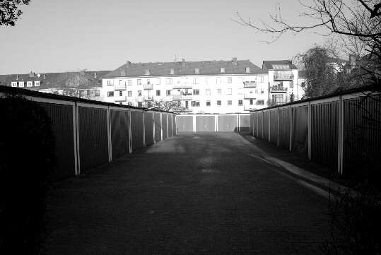 Rear of a big block of flats, in the foreground backyard garages