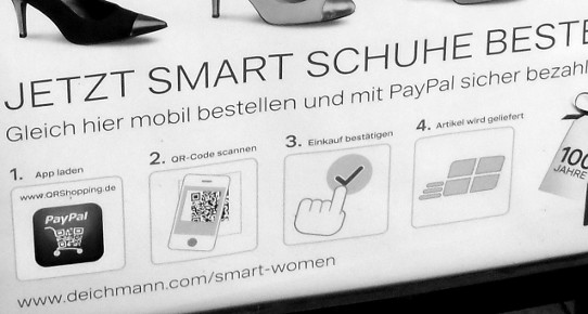 Ausschnitt aus Plakat in Bremen, das es Menschen ermöglicht mit Hilfe eines gut ausgestatteten Mobiltelefons Schuhe zu bestellen